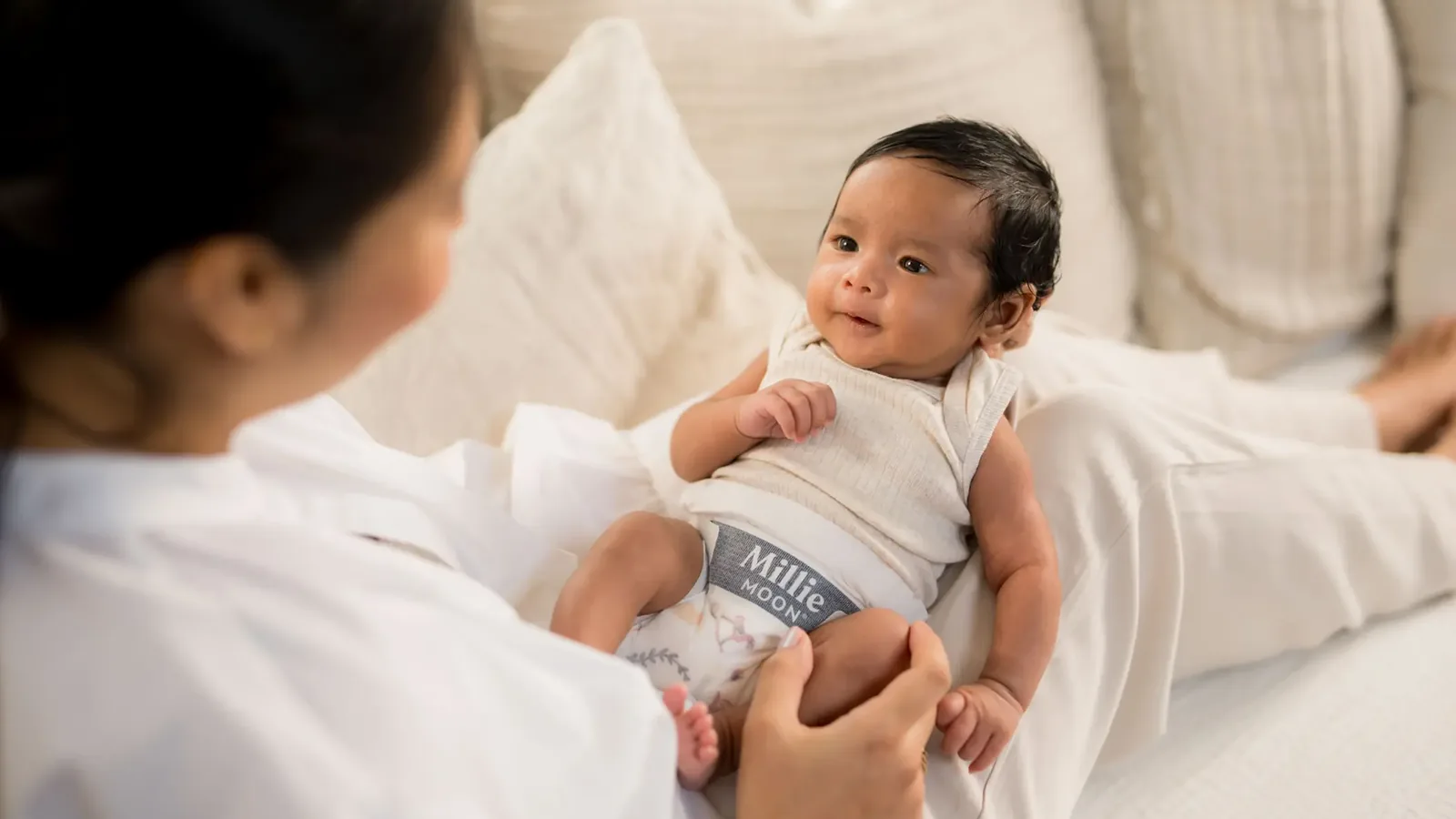 A parent holding a smiling baby in a nappy on a bed