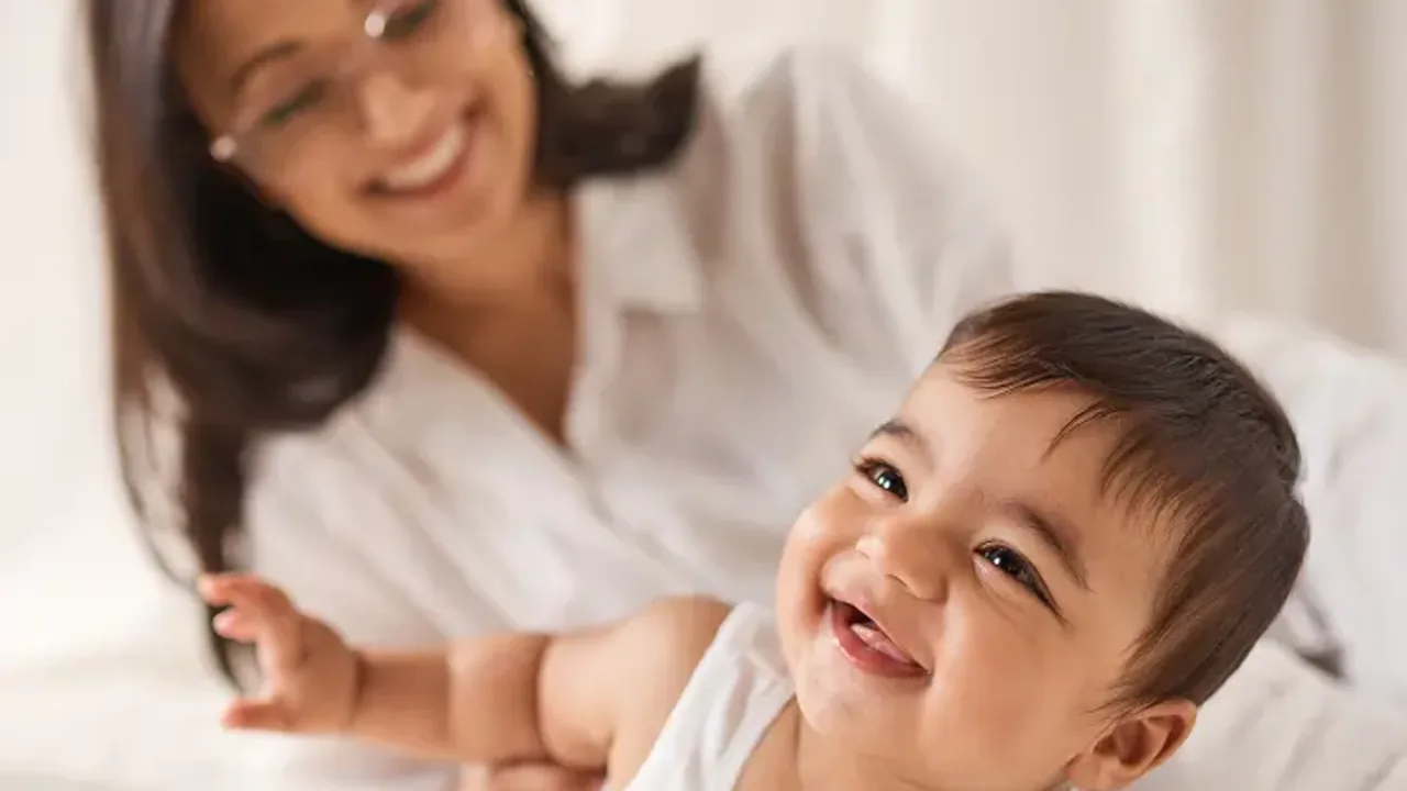 A parent smiling at a baby lying on a bed