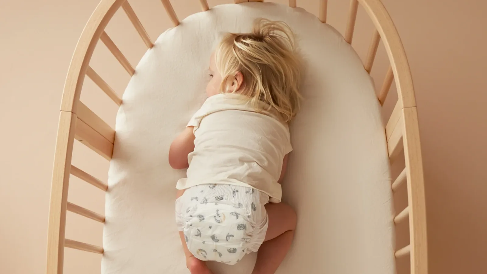 A toddler asleep on their front in a wooden cot