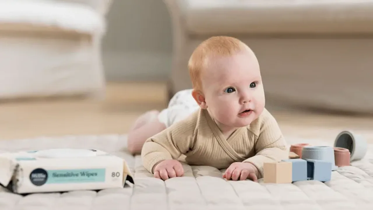 A baby lying on their front on a play mat beside a pack of wipes
