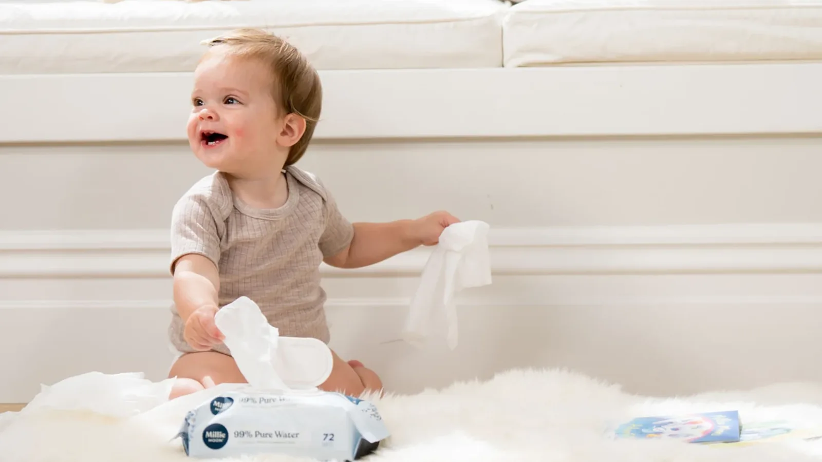 A sitting toddler playing with wipes on a sheepskin rug