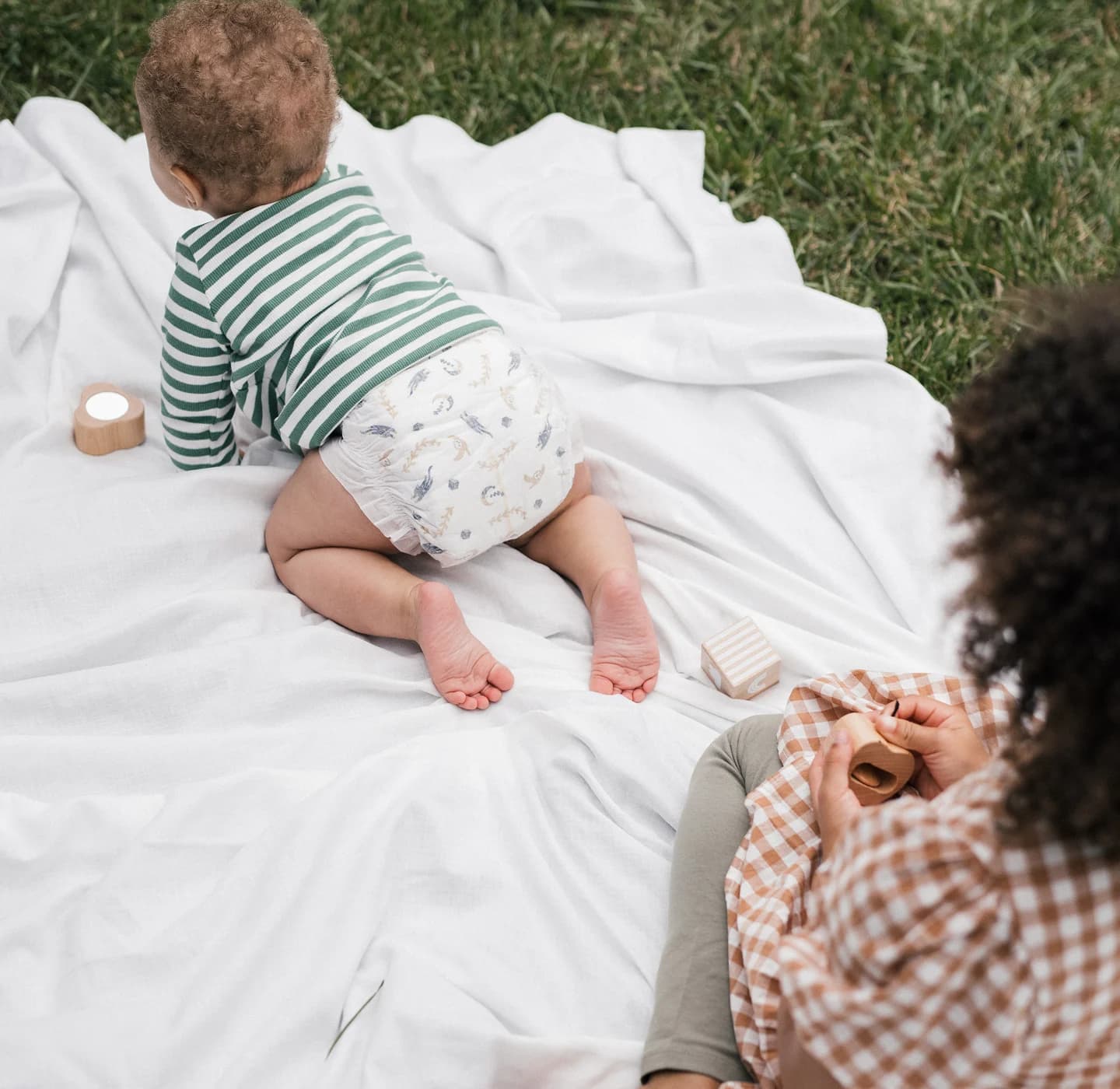 Baby in a Millie Moon tape diaper crawling on a picnic blanket beside a parent