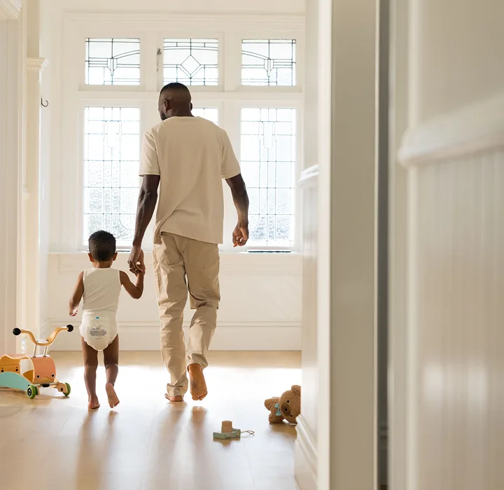 Parent walking hand in hand down a sunlit hallway with a toddler in a Millie Moon tape diaper