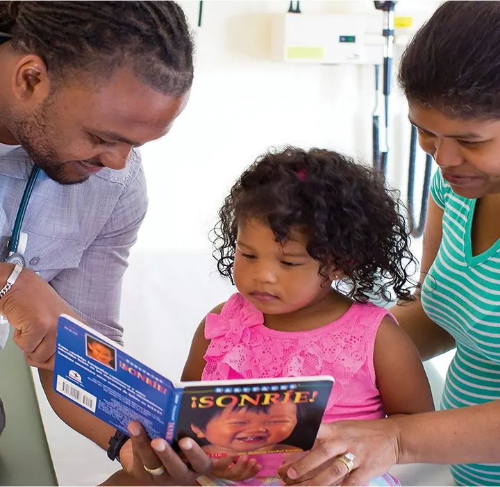 Reach Out and Read clinician sharing a picture book with a toddler and their parent during a check-up