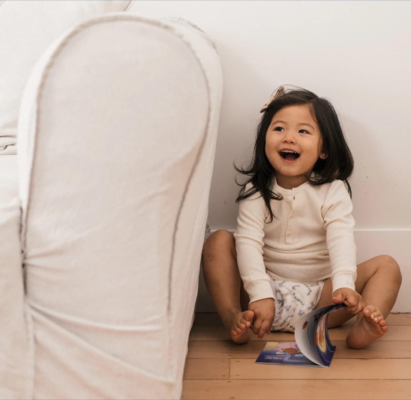 Laughing toddler in a Millie Moon diaper sitting on the floor with an open Millie Moon storybook