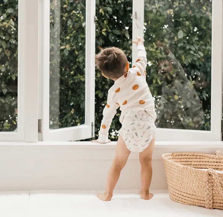 Toddler in a Millie Moon tape diaper reaching up towards an open window