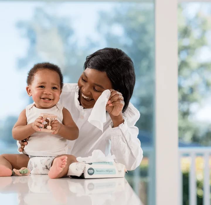 Parent using a Millie Moon Sensitive Wipe to clean a smiling baby's hands