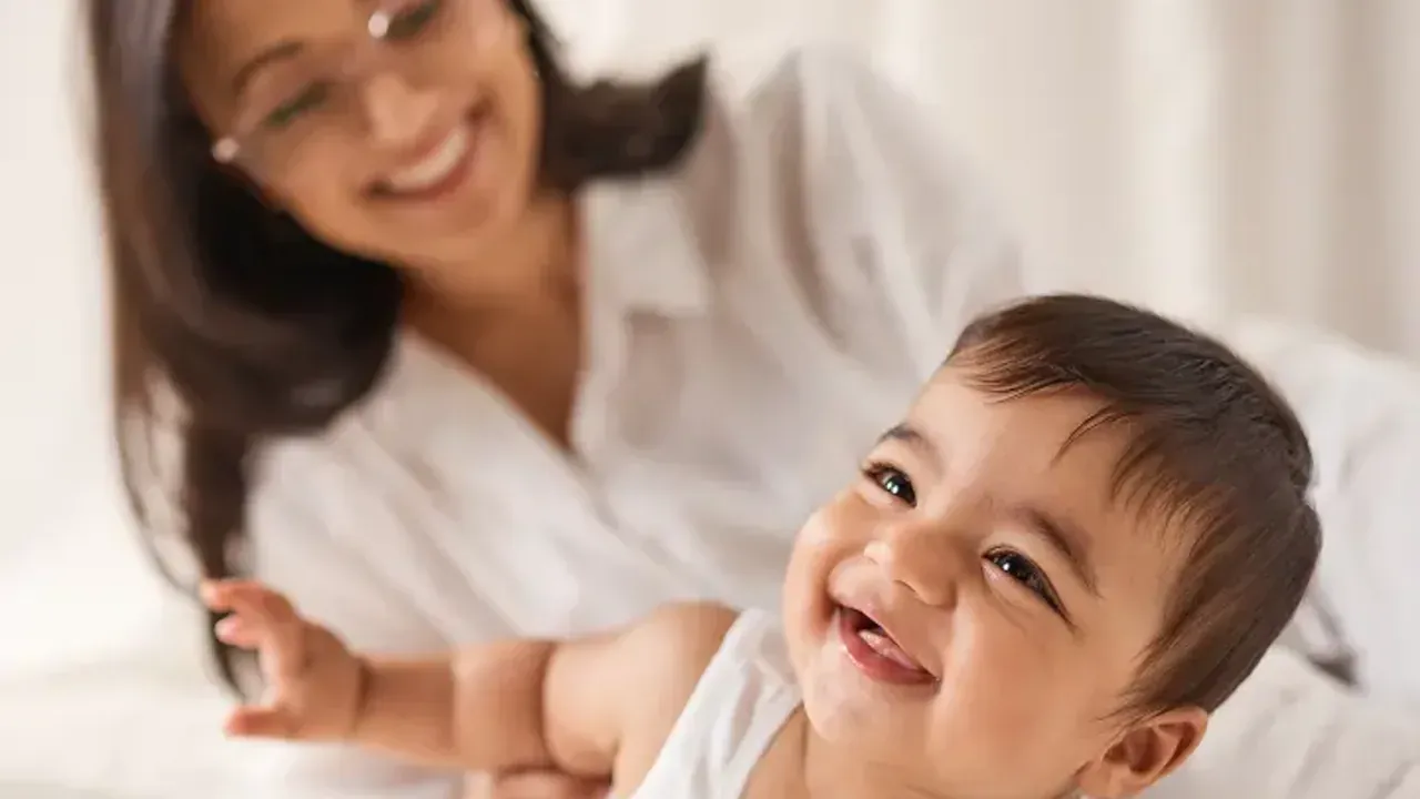 A parent smiling at a baby lying on a bed